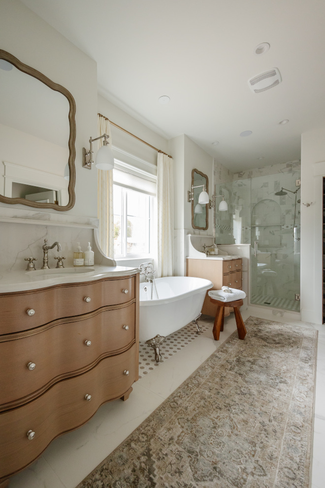 Dresser looking custom vanities along with a clawfoot tub add a feminine and a vintage feel to this neutral primary bathroom #Dresserlookingvanity #clawfoottub #vintagefeel #neutralprimarybathroom