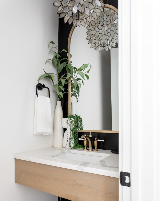 A floating white oak vanity accentuated by a black shiplap accent wall along with a curved brass mirror and striking pendant light create a powder bath that is sure to impress #floatingvanity #floatingwhiteoakvanity #blackshiplap #accentwall #curvedbrassmirror #powderbath