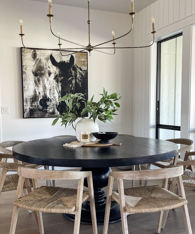 A large round black dining table is complemented by oak dining chairs with hand-woven seagrass seats #roundblackdiningtable #blackdiningtable #diningtable #oakdiningchairs #diningchairs #handwovenseagrassseat
