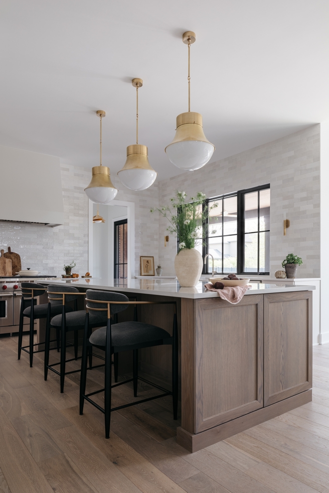 Warm white perimeter cabinets in Sherwin Williams Heron Plume along with a grey oak island brass accents and textures tiles from counter to ceiling create a sense of coziness and belonging without compromising on style in this kitchen #SherwinWilliams #SherwinWilliamsHeronPlume #kitchen