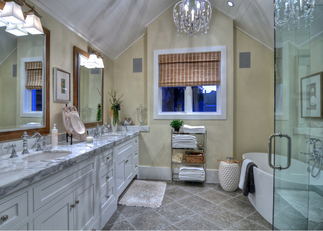 Bathroom. Bathroo Design. This master bathroom has unique details from floor to ceiling. A hanging chandelier draws the eye to the peaked ceiling which gives the room an open feel. Tones of tan, gold, gray and white create a clean look, accessorized with subtle coastal decor. The large, deep, freestanding bathtub is the perfect place to unwind and relax. #Bathroom #BathroomDesign