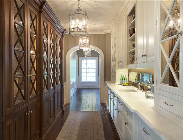 Butler's Pantry with plenty of cabinets and Calacatta marble counters. This is an extraordinary butler's pantry design, with Calacatta marble countertop, white glass-front cabinets and lantern pendant lighting. Lantern Pendants are the "Visual Comfort CHC3421BZ Chart House 4 Light Small Arch Top Lantern". #ButlersPantry #Pantry #CabinetDesign Designed by Yunker Associates Architecture.