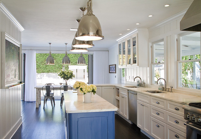 Kitchen. Bright, modern kitchen with white cabinets, glass front cabinets, metal chairs, pendant lighting, hardwood floors, white wood walls, silver pendants, white crown moulding, chrome hardware, white wood paneling and dark hardwood floors. #Kitchen #KitchenDesign #Kitchenideas