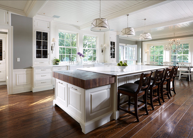 Large, spacious kitchen design with glass-front white kitchen cabinets, white kitchen island with lots of storage, marble countertops, wodden paneling backsplash, double apron sink and gray walls paint color. Hardwood flooring is white oak. #KitchenDesign #WhiteKitchen Designed by Yunker Associates Architecture. 