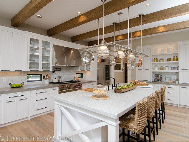 Transitional Kitchen. Transitional White Kitchen Design. Kitchen. Transitional kitchen with custom lighted pot rack, rustic beams, custom stainless steel hood, glass cabinet doors, v-groove cabinet doors, subzero fridge, wolf range, Carrera marble island, apron sink, windows backsplash, marble splash subway tile splash, hardwoods, glass shelves, pot filler, under cabinet lighting.